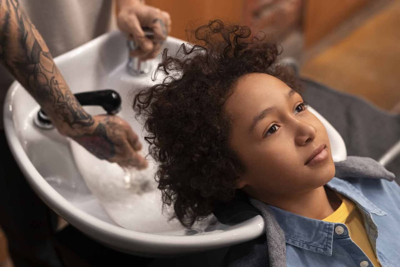 Imagem de um jovem modelo de cabelos cacheados médios, em um assento para lavagem de cabelo em um salão