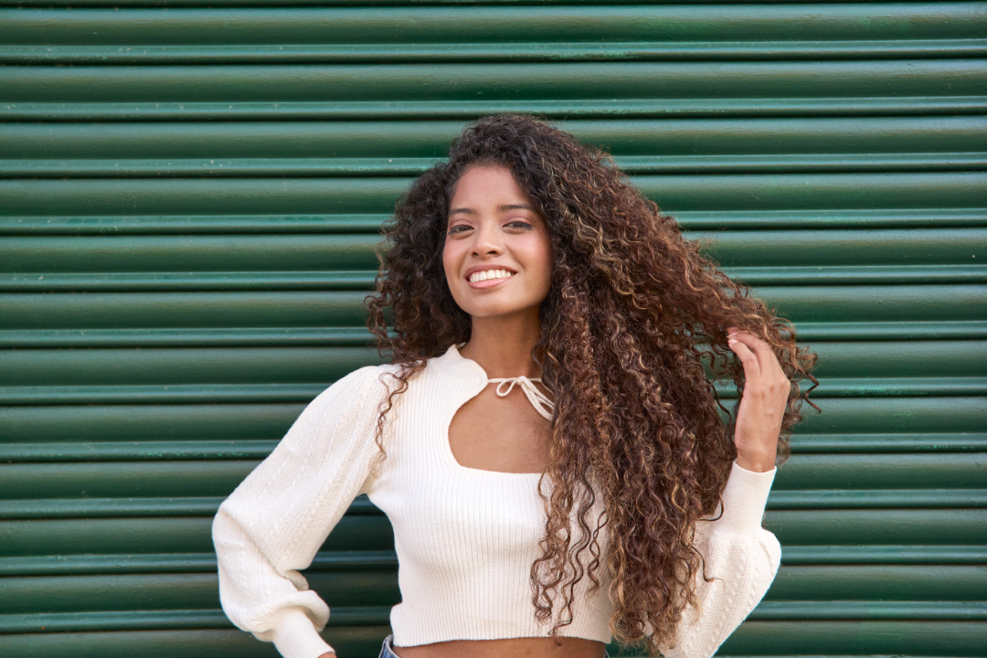 Mulher com cabelo cacheado sorrindo em fundo verde.